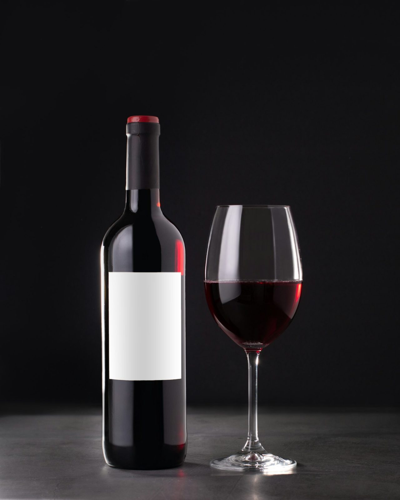 single red wine bottle with blank label for mockup and glass of red wine on dark gray background